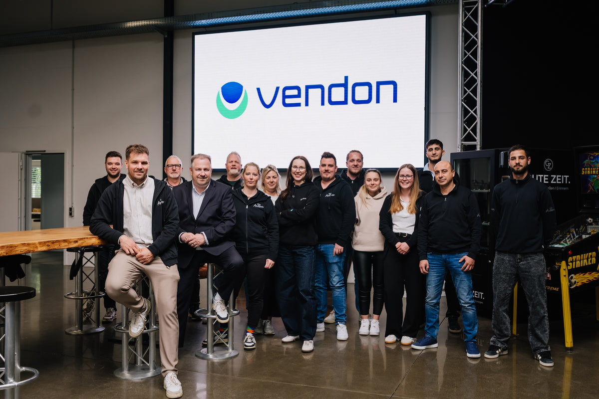 Team von Vendon vor großem Bildschirm mit Logo, moderne Automaten im Hintergrund