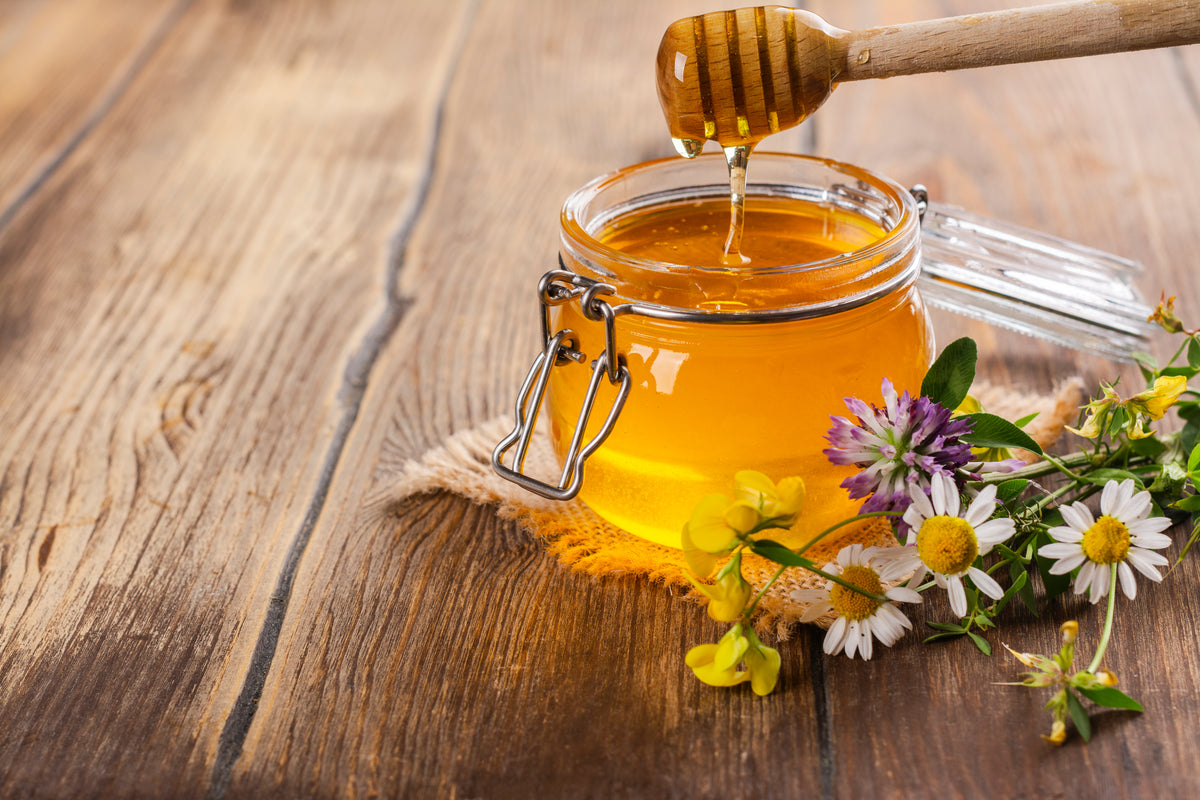 Honig aus Glasgefäß mit Holzlöffel und Blumen auf Holztisch