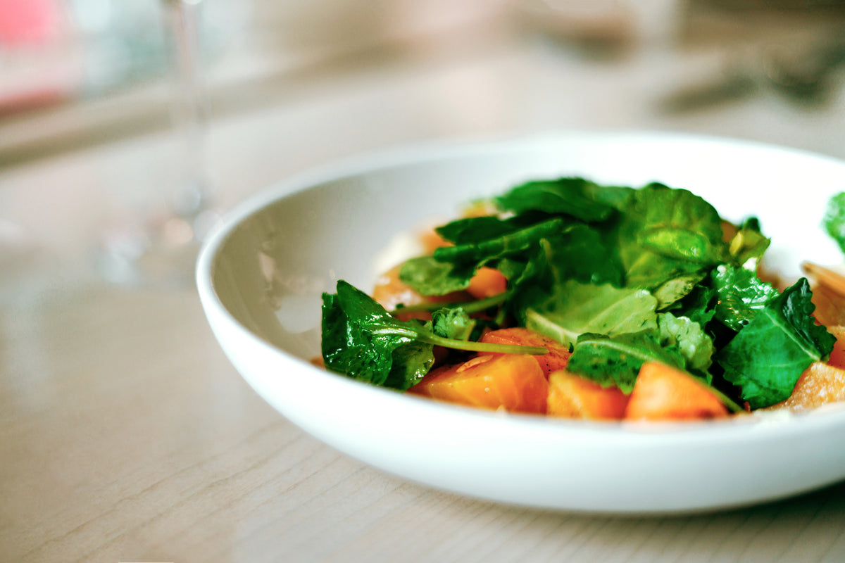 Nahaufnahme eines frischen Salats mit grünem Blattgemüse und orangefarbenen Tomaten in einer weißen Schüssel