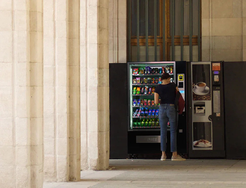 Person vor Getränke- und Snackautomat in urbaner Umgebung